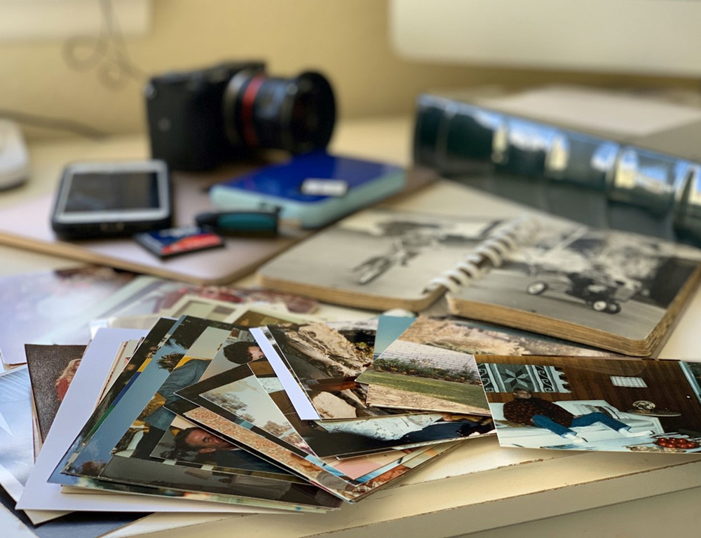 A workspace with printed family photos, albums, a camera and a backup drive