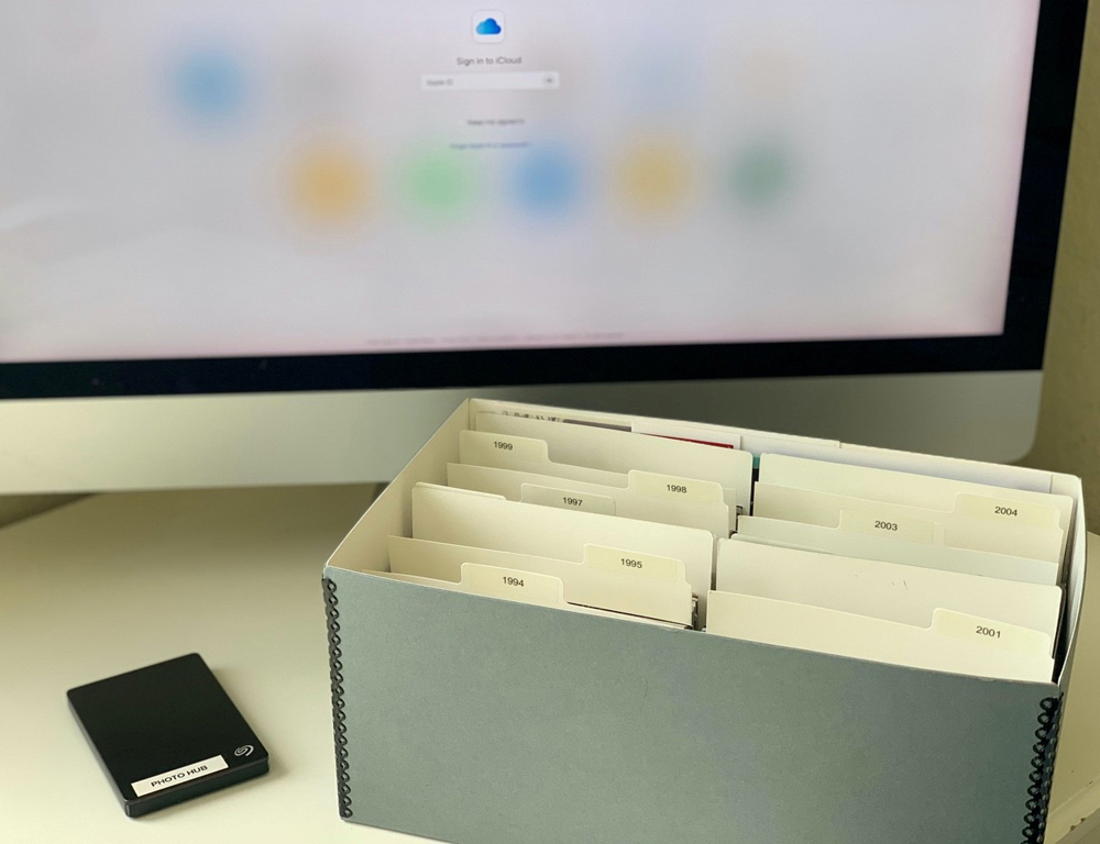 Archival photo box with year dividers next to a backup drive